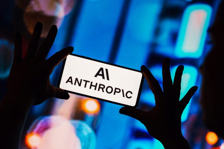 Hands holding smartphone displaying AI Anthropic text against blue digital technology background